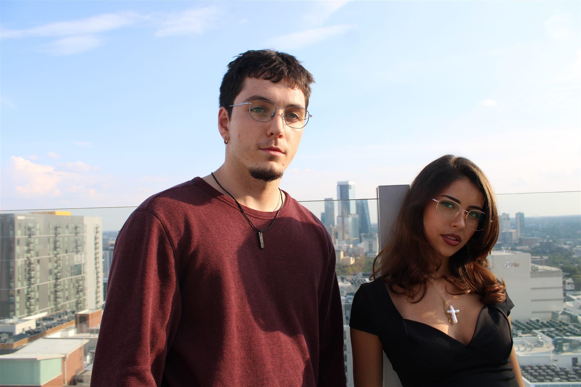 Two people wearing glasses on a rooftop with the city skyline behind them